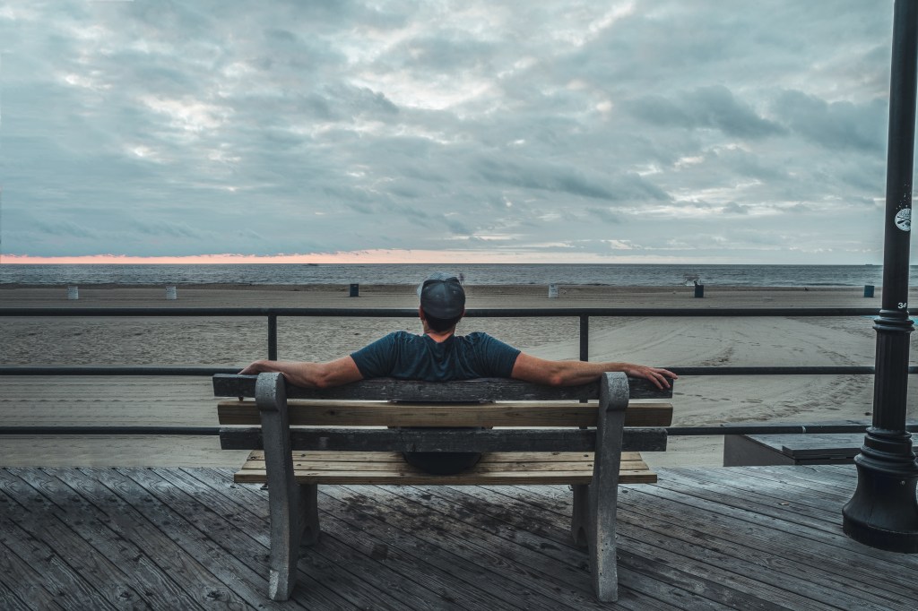 Andrew Wolff sitting on a bench overlooking the ocean in Asbury Park reflective coastal photography