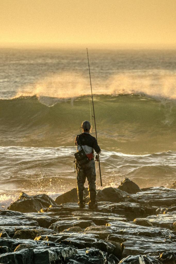 Fisherman standing on rocks as waves crash during golden hour