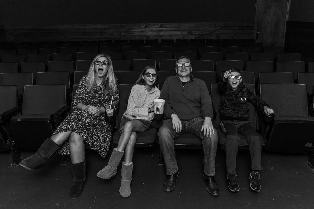 Family enjoying a movie together in a theater wearing 3D glasses, black and white candid photography.