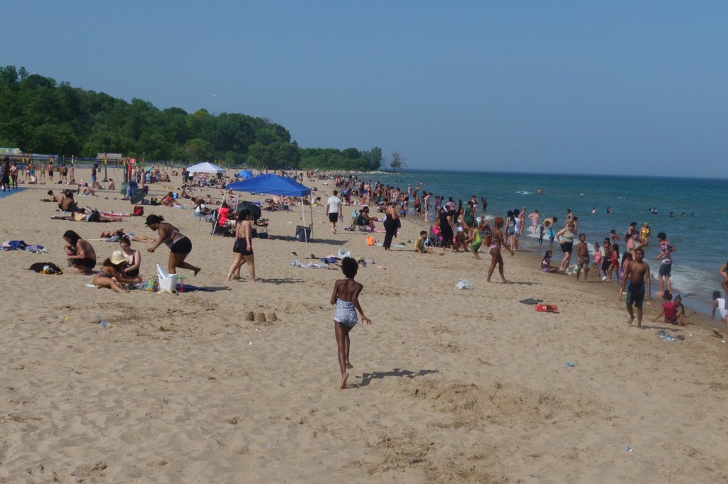 Before-and-after comparison of the same Lake Michigan beach scene. The original photograph shows a crowded beach with many people, while the edited version features a single child running along an otherwise empty shoreline, illustrating how removing distractions can change the mood and storytelling of a photograph.